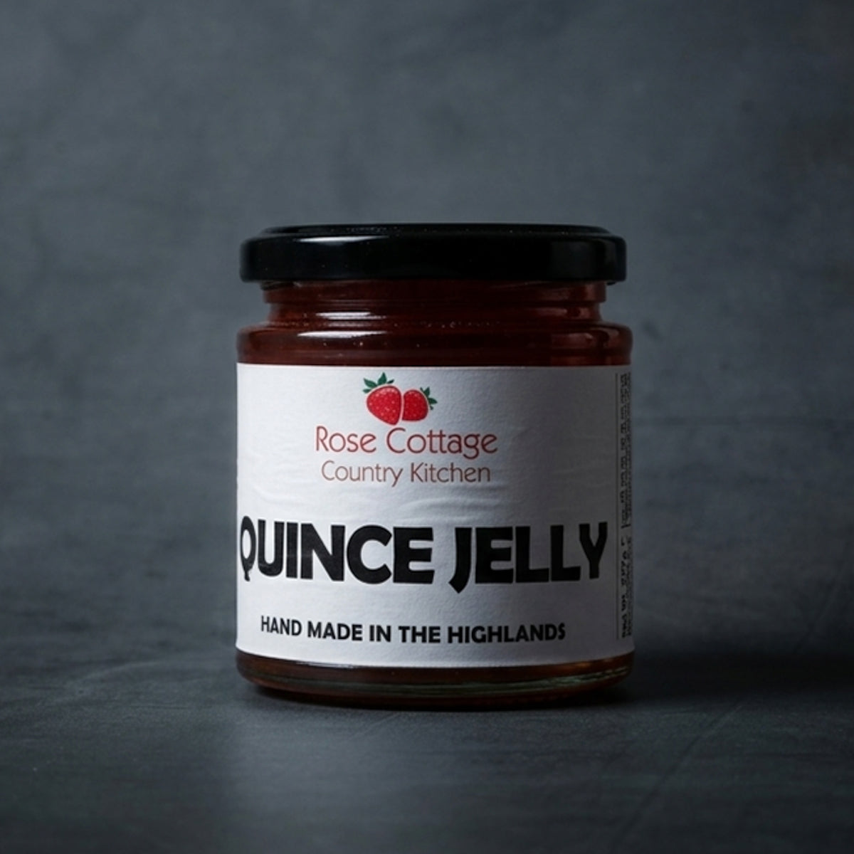 A jar of handmade quince jelly from Rose Cottage Country Kitchen, labeled "Hand Made in the Highlands," displayed on a dark grey textured surface.